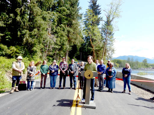 Gov. Bob Ferguson addresses the crowd at the Upper Hoh Road washout repair on Thursday afternoon. Local officials, business owners, contractors, workers from the Jefferson County Public Works department and a few individuals who donated funds to the project stand behind him. Before the ribbon was cut and the road officially opened, there were short statements from involved parties. Ferguson said he brought his hiking boots and joked that he wanted to be the first one to hit the trail. (Christi Baron/Olympic Peninsula News Group)