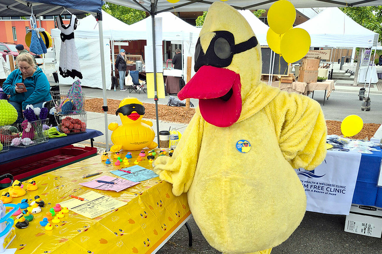 Volunteer Pam Scott dresses the part as she sells ducks for the Great Olympic Peninsula Duck Derby at the Sequim Farmers and Artisans Market on Saturday. (Leah Leach/for Peninsula Daily News)