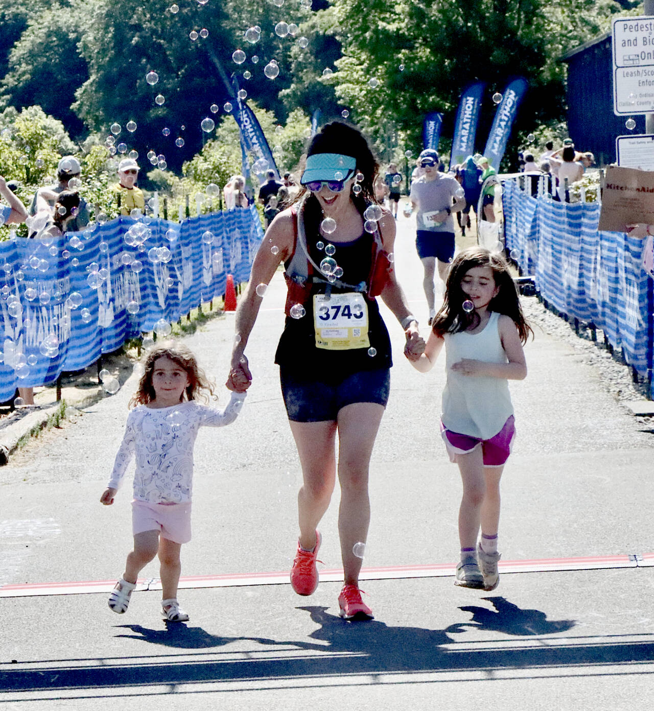 Ivy Karlinsky of Seattle has her two daughters Isla, 6, and Ellie, 3, help her over the finish line during the last 20 meters of her half-marathon race at the Port Angeles Pier on Sunday. (Dave Logan/for Peninsula Daily News)