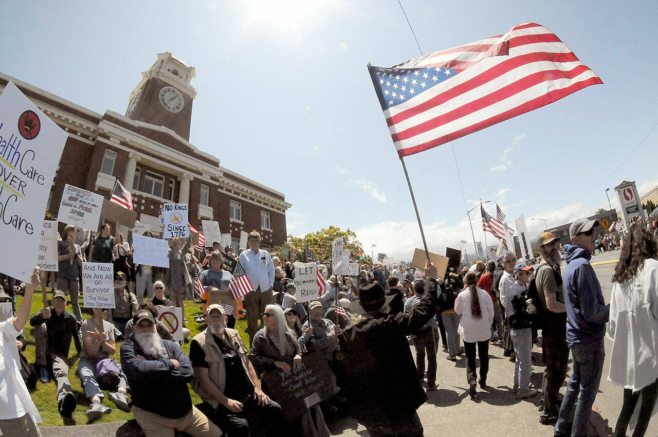 A demonstrator carrying an American flag walks the sidewalk in front of the Clallam County Courthouse on Saturday. (Keith Thorpe/Peninsula Daily News)