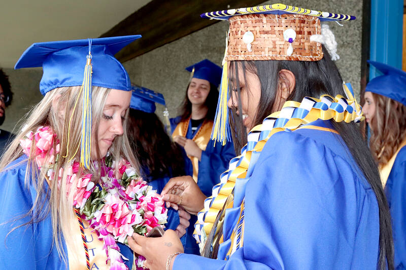 Crescent School senior Audrey Gales, right, looks at the homemade regalia worn by fellow senior Hayden Horn on Saturday. Gales had a handmade Native American cap ready for her graduation. Seventeen Crescent students graduated during traditional ceremonies in the school gym. (Dave Logan/for Peninsula Daily News)