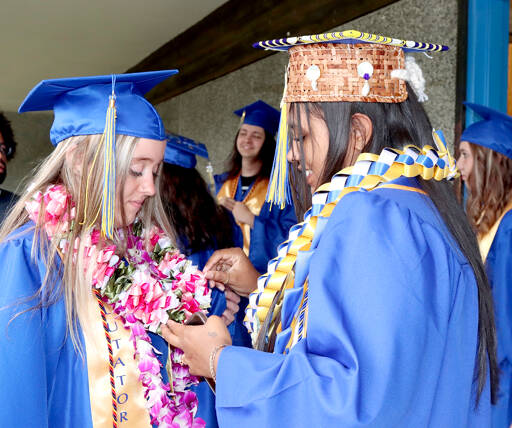 Crescent School senior Audrey Gales, right, looks at the homemade regalia worn by fellow senior Hayden Horn on Saturday. Gales had a handmade Native American cap ready for her graduation. Seventeen Crescent students graduated during traditional ceremonies in the school gym. (Dave Logan/for Peninsula Daily News)