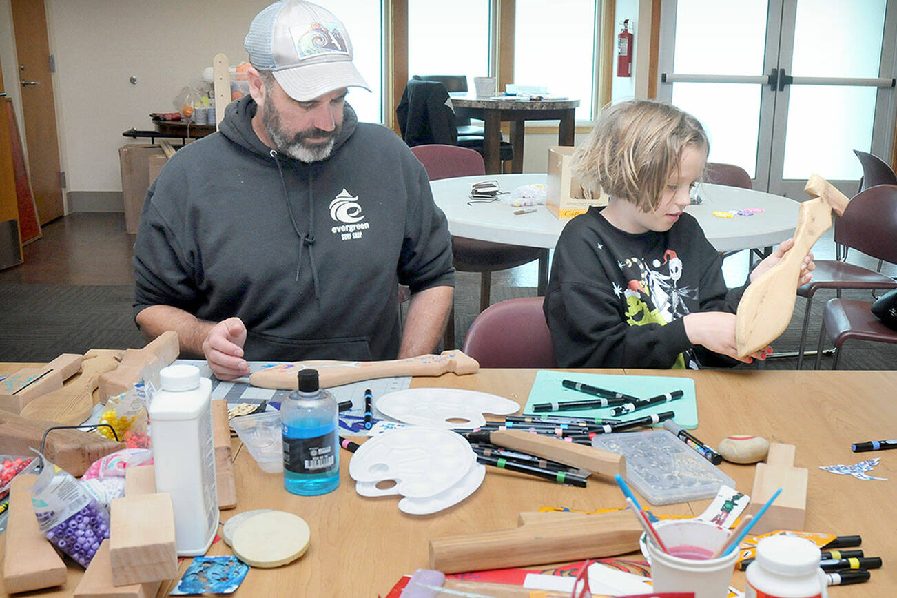 KEITH THORPE/PENINSULA DAILY NEWS
June Ward, 10, examines a wooden paddle she is decorating as her father, Jack Ward of Port Angeles, works on his own paddle during a craft-making session on Friday at the Elwha Klallam Heritage Center in Port Angeles. The paddles are among the thousands of gifts being created for participants in the 2025 Tribal Canoe Journey, hosted this year by the Lower Elwha Klallam Tribe. The event begins with the landing of dozens of native canoes at the mouth of the Elwha River on July 31 and continues with five days of celebration on the Lower Elwha reservation west of Port Angeles. As many as 10,000 indigenous peoples are expected to take part. The public is invited to help with giftmaking sessions, scheduled daily from 9 a.m. to 4 p.m. at the Heritage Center.