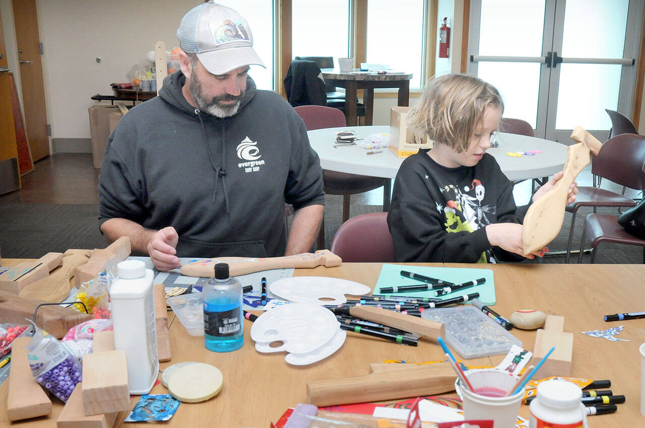 June Ward, 10, examines a wooden paddle she is decorating as her father, Jack Ward of Port Angeles, works on his own paddle during a craft-making session on Friday at the Elwha Klallam Heritage Center in Port Angeles. The paddles are among the thousands of gifts being created for participants in the 2025 Tribal Canoe Journey, hosted this year by the Lower Elwha Klallam Tribe. The event will begin with the landing of dozens of native canoes at the mouth of the Elwha River on July 31 and continues with five days of celebration on the Lower Elwha reservation west of Port Angeles. As many as 10,000 indigenous peoples are expected to take part. The public is invited to help with giftmaking sessions, scheduled daily from 9 a.m. to 4 p.m. at the Heritage Center. (KEITH THORPE/PENINSULA DAILY NEWS)