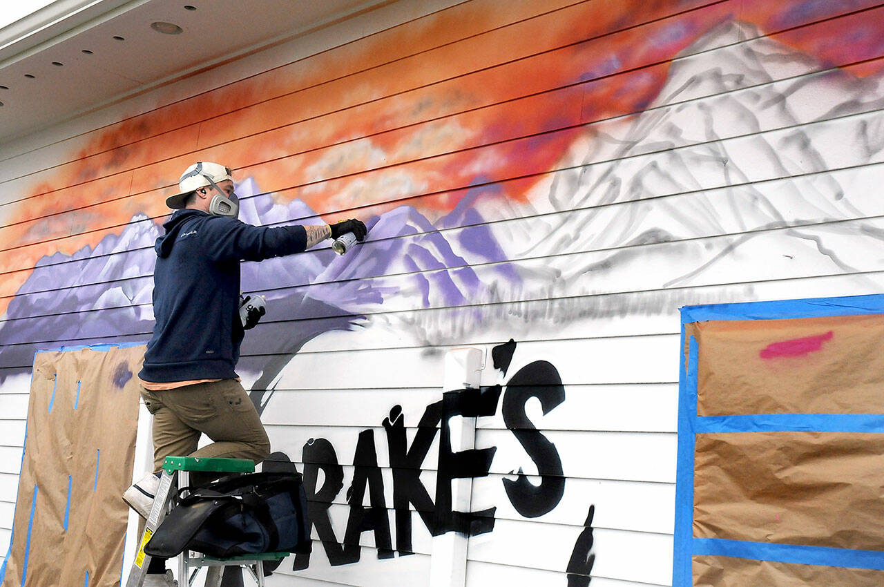 Muralist Adam Nelson of Port Angeles paints a mountainscape on the north wall of Drake’s U-Bake Pizza & Subs on Wednesday in Port Angeles. Nelson said the job would take about two days to complete. (Keith Thorpe/Peninsula Daily News)