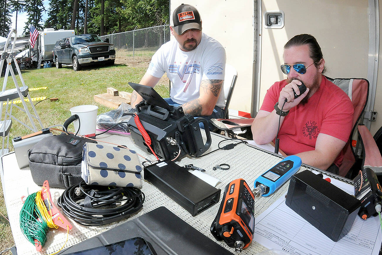 Amateur radio operator Tyler Tenneson of Port Angeles, who uses the radio call sign WA7TCT, left, watches as fellow operator Patrick Singhose of Port Angeles, call sign W7PGS, makes radio contact with other radio stations during Saturday’s ARRL Field Day from a temporary station at the Clallam County Fairgrounds. During the event, participants attempt to make radio contact with as many other operators scattered across North America and around the world from self-contained stations, simulating conditions that may occur in an emergency. Field Day, sanctioned by the American Radio Relay League, also serves as an open house for the pubic to witness, and in some cases, take part in the world of amateur radio. (Keith Thorpe/Peninsula Daily News)