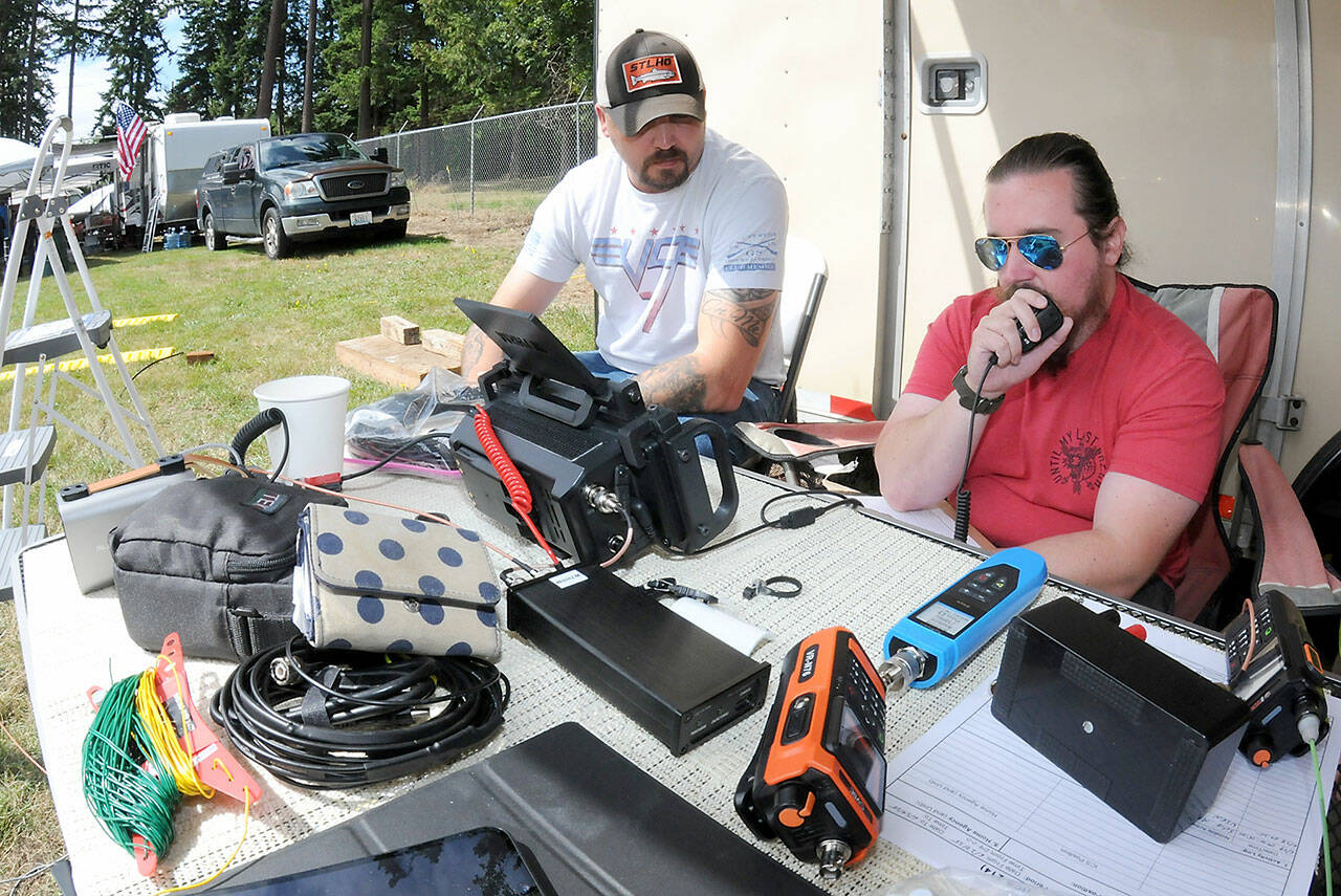 Amateur radio operator Tyler Tenneson of Port Angeles, who uses the radio call sign WA7TCT, left, watches as fellow operator Patrick Singhose of Port Angeles, call sign W7PGS, makes radio contact with other radio stations during Saturday’s ARRL Field Day from a temporary station at the Clallam County Fairgrounds. During the event, participants attempt to make radio contact with as many other operators scattered across North America and around the world from self-contained stations, simulating conditions that may occur in an emergency. Field Day, sanctioned by the American Radio Relay League, also serves as an open house for the pubic to witness, and in some cases, take part in the world of amateur radio. (Keith Thorpe/Peninsula Daily News)