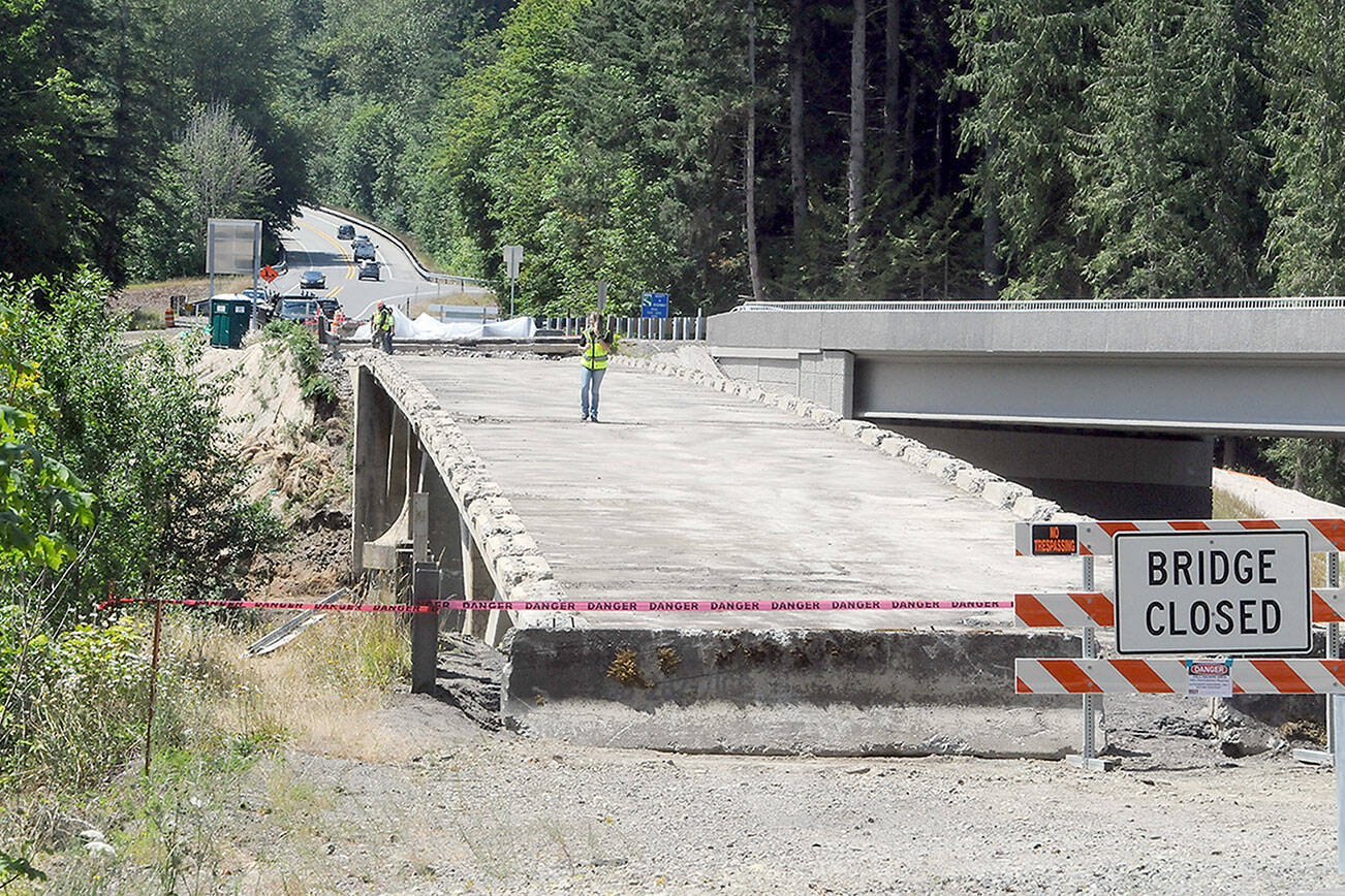 KEITH THORPE/PENINSULA DAILY NEWS
Construction workers stand on what remains of the old U.S. 101 bridge over the Elwha River on Wednesday as the aging structure is dismantled. The old bridge, built in 1926, was in danger of washout when the river beneath changed course and engineers discovered the bridge piers were built on gravel instead of bedrock, leading to constructon of a new bridge, at right, which was opened to traffic in 2024. The old bridge was to remain in place until a fish-spawning window, which runs from mid-July until the end of August.