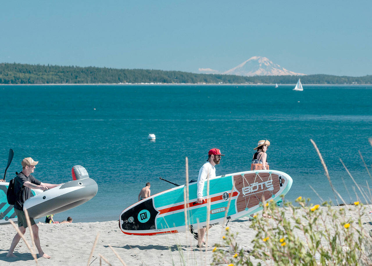 Beachgoers look for a spot on the sand on Sunday afternoon at Fort Worden State Park in Port Townsend. Mount Rainier looms in the distance. (Steve Mullensky/for Peninsula Daily News)