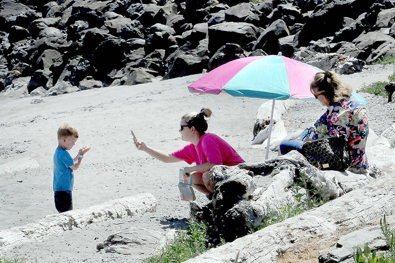 Lisa Hansen of Port Angeles, center, takes a cellphone photo of her son, Cooper Hansen, 3, as Hansen’s mother, Tracy Hansen, right, looks on during a warm day at Hollywood Beach on the Port Angeles waterfront on Wednesday. The trio were enjoying a sunny summer afternoon next to the water. (Keith Thorpe/Peninsula Daily News)