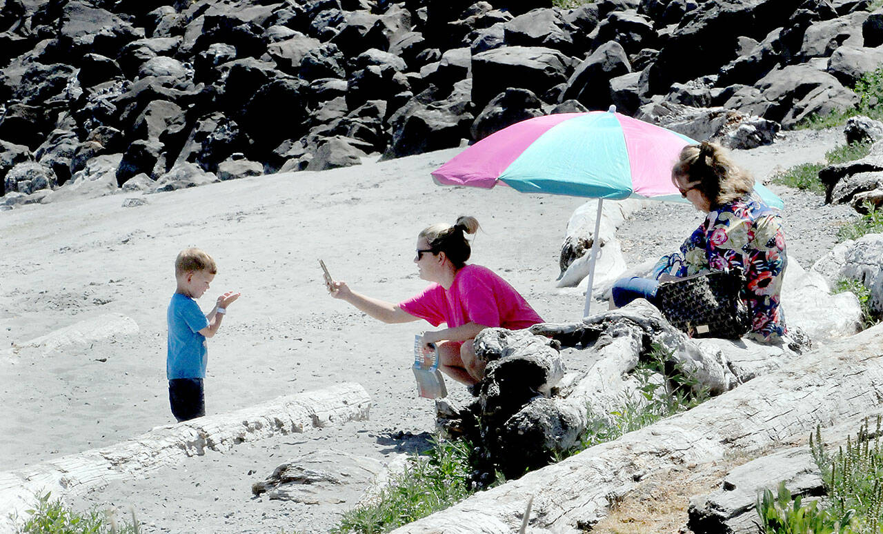 Lisa Hansen of Port Angeles, center, takes a cellphone photo of her son, Cooper Hansen, 3, as Hansen’s mother, Tracy Hansen, right, looks on during a warm day at Hollywood Beach on the Port Angeles waterfront on Wednesday. The trio were enjoying a sunny summer afternoon next to the water. (Keith Thorpe/Peninsula Daily News)