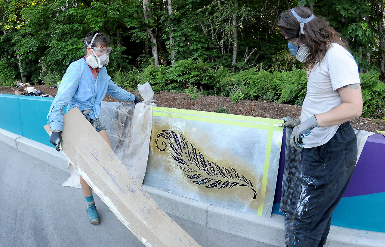 Artists Heather Sparks, left, and Zeo Boekbinder set up a stencil of a fern leaf in an effort to decorate an otherwise-drab concrete roadside divider along Race Street south of Lauridsen Boulevard on Wednesday in Port Angeles. The divider work was part of a larger project to beautify the Race Street corridor from Eighth Street to Hurricane Ridge Road, which included improved traffic lanes, pedestrian and bicycle lanes and decorative lighting. Long-term plans call for similar improvements to Race Street, extending to First and Front streets. (Keith Thorpe/Peninsula Daily News)