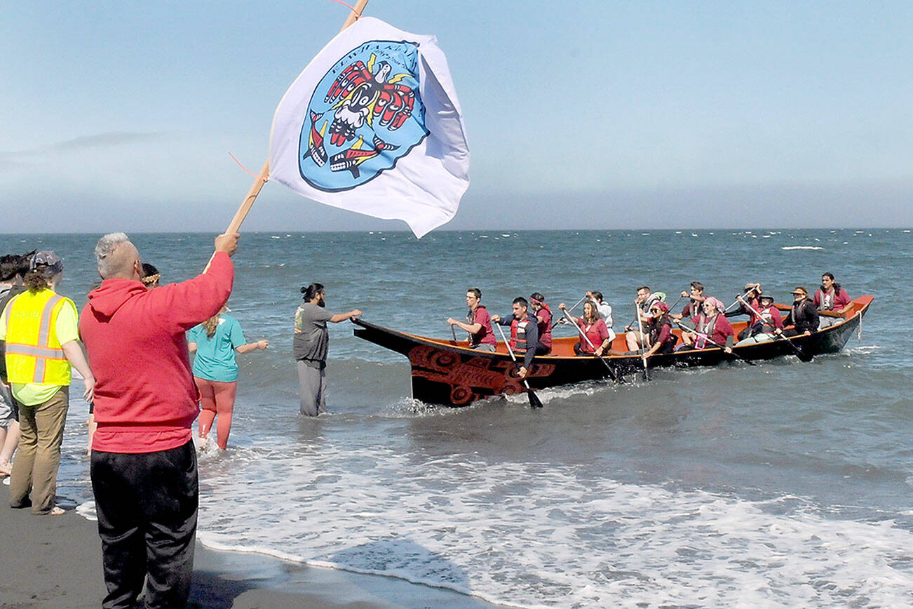 Tribal member Jerry Foster waves a Lower Elwha Klallam tribal flag as a canoe paddled by members of the Port Gamble S’Klallam Tribe arrives at Elwha Beach at Angeles Point on Thursday. (Keith Thorpe/Peninsula Daily News)