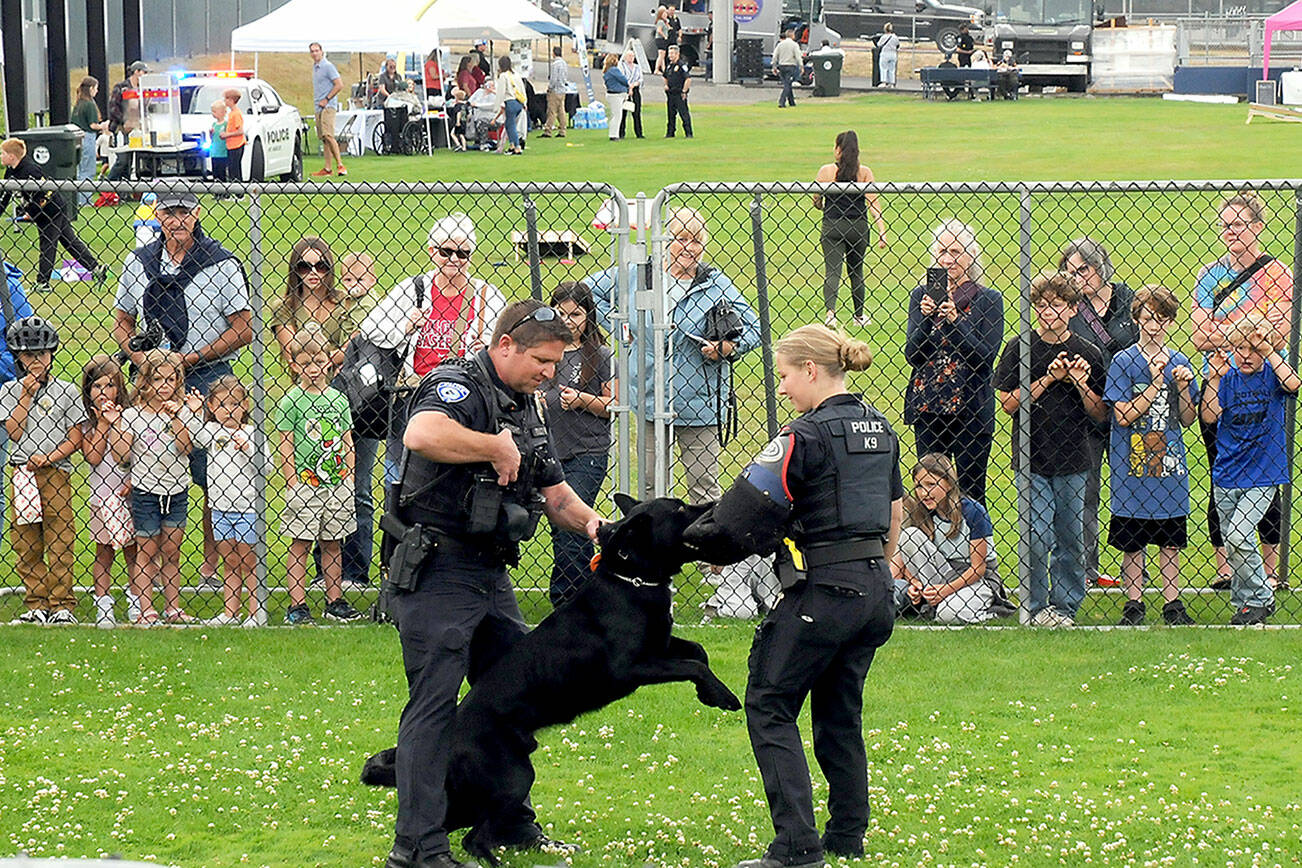 Port Angeles Police officers Kenneth McKnight, left, and Lilliana Emery give a canine demonstration with Freddy, a trained police dog, during Tuesday’s National Night Out at Port Angeles Civic Field. The nationwide event brought law enforcement agencies, watch groups and civic organizations together for an evening of community building, featuring informational displays, children’s activities and a large-screen movie presentation. (Keith Thorpe/Peninsula Daily News)