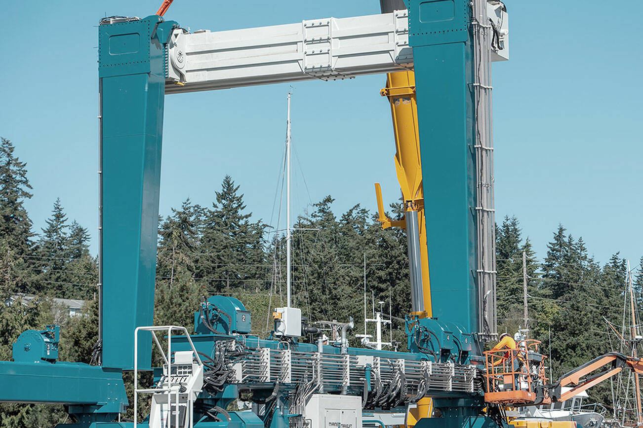 Still suspended and held in steady by a heavy lift crane, a 50-ton crossmember beam of the new 300-ton variable width Travelift acquired by the Port of Port Townsend is bolted down by an employee, lower right, on Monday. (Steve Mullensky/for Peninsula Daily News)