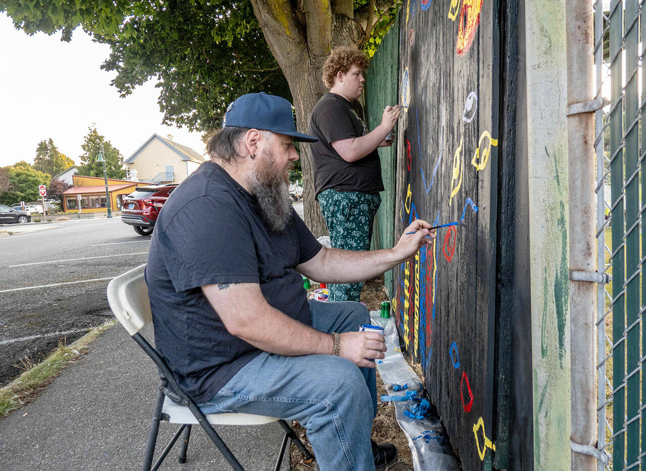 Jesse Adams, front, of Port Townsend, and son Evan of Allyn paint eyes on a section of the fence surrounding Port Townsend’s Memorial Field as their contribution to the Outsiders Street Art Project Port Townsend during Jefferson County’s first community public art project. Adams’ project, titled “Eye Strain,” had to be submitted for approval before work could begin. Each artist had an 8-foot section of fence to work on. The fence will be taken down, most likely next spring, to be replaced with a new one. (Steve Mullensky/for Peninsula Daily News)