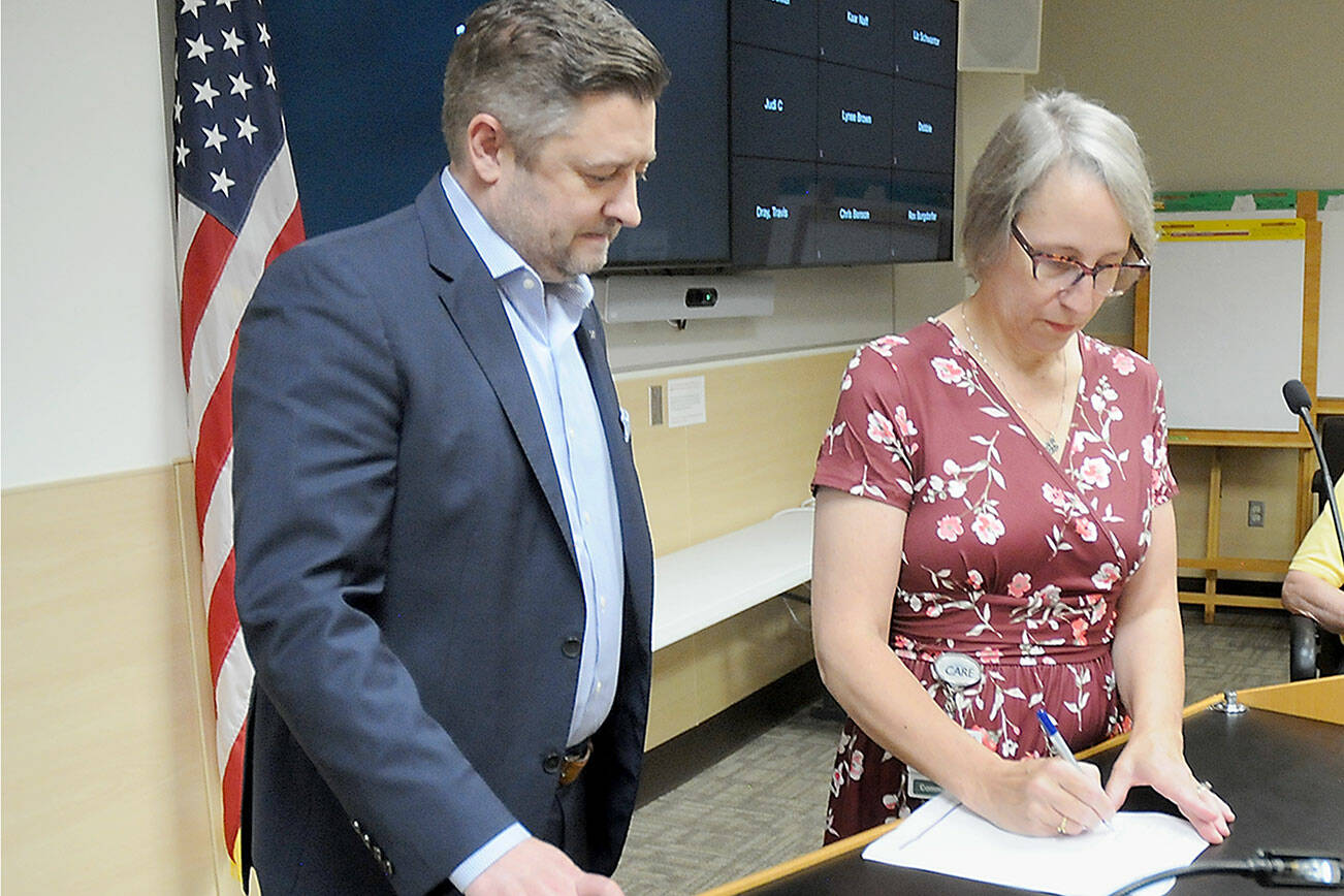 Brad Simmons, president of UW Medicine Hospitals & Clinics, left, looks on as Olympic Medical Center Board President Ann Henninger signs a letter of intent on Wednesday to pursue an operating agreement between the two organizations. (Keith Thorpe/Peninsula Daily News)