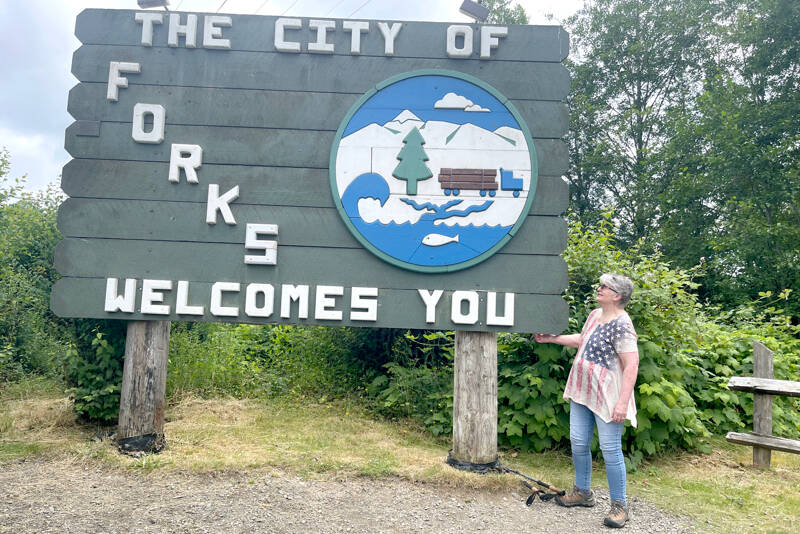 Mary Engel Springer Donovan stands next to the Welcome to Forks sign she designed in 1986. (Christi Baron/Olympic Peninsula News Group)