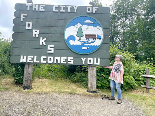 Mary Engel Springer Donovan stands next to the Welcome to Forks sign she designed in 1986. (Christi Baron/Olympic Peninsula News Group)