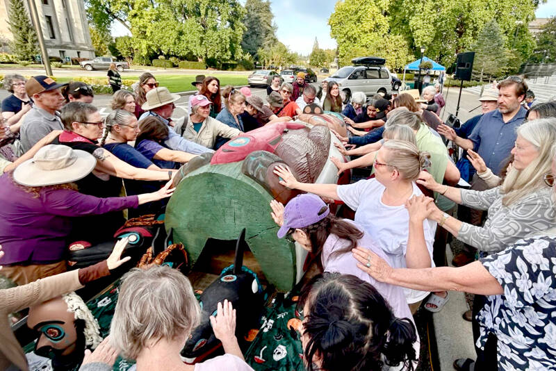A crowd of about 120 people bless a totem pole and 10 cedar masks carved by the Lummi Nation’s House of Tears outside of the Capitol building in Olympia on Monday as part of the Indigenous-led campaign “Xaalh and the Way of the Masks.” The totem and masks will travel 1,700 miles between rally sites in Washington and Oregon before it’s given to the Lower Elwha Klallam Tribe west of Port Angeles on Sept. 20. (Emily Fitzgerald/Washington State Standard)