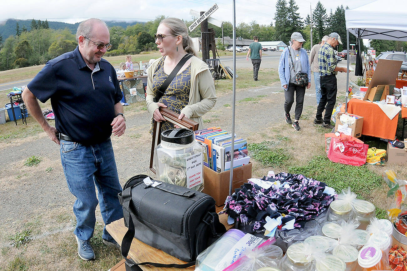 Tim Blair and Amy Peterson, both of Port Townsend, make a purchase from a table of random sale items during Saturday’s Great Strait Sale at a community vending location in Joyce. The annual event featured dozens of yard and garage sales stretching along state Highway 112 from Port Angeles to Neah Bay. (Keith Thorpe/Peninsula Daily News)