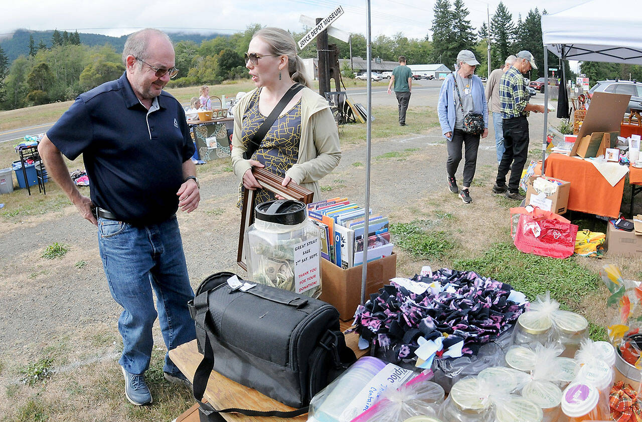 Tim Blair and Amy Peterson, both of Port Townsend, make a purchase from a table of random sale items during Saturday’s Great Strait Sale at a community vending location in Joyce. The annual event featured dozens of yard and garage sales stretching along state Highway 112 from Port Angeles to Neah Bay. (Keith Thorpe/Peninsula Daily News)