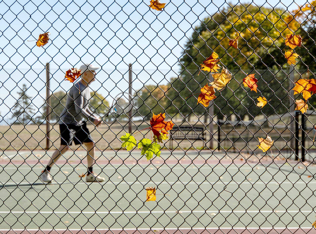 Fallen leaves cling to a fence as Chris White of Port Townsend sets up for a forehand volley during a tennis match at the Fort Worden tennis courts on Thursday. (Steve Mullensky/for Peninsula Daily News)