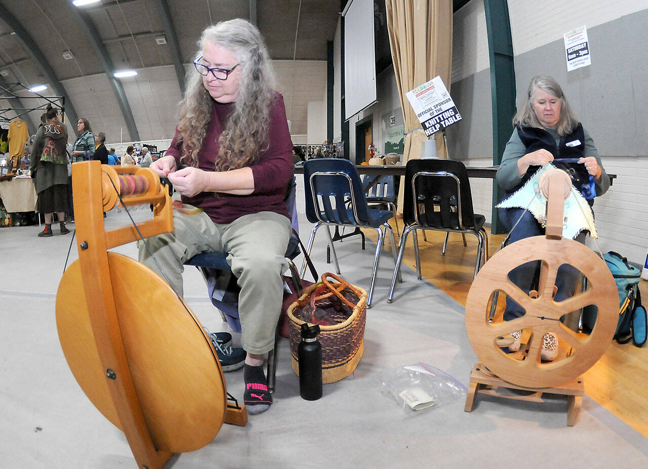 Sarah Severns, left, and Diana Burns, both of Sequim and members of the North Olympic Shuttle & Spindle Guild, operate a pair of spinning wheels at a demonstration table at the Pacific Northwest Fiber Arts Expo on Friday at Vern Burton Community Center in Port Angeles. The three-day festival featured dozens of vendor displays, workshops and demonstrations that supported knitting, weaving and other fiber activities. (Keith Thorpe/Peninsula Daily News)