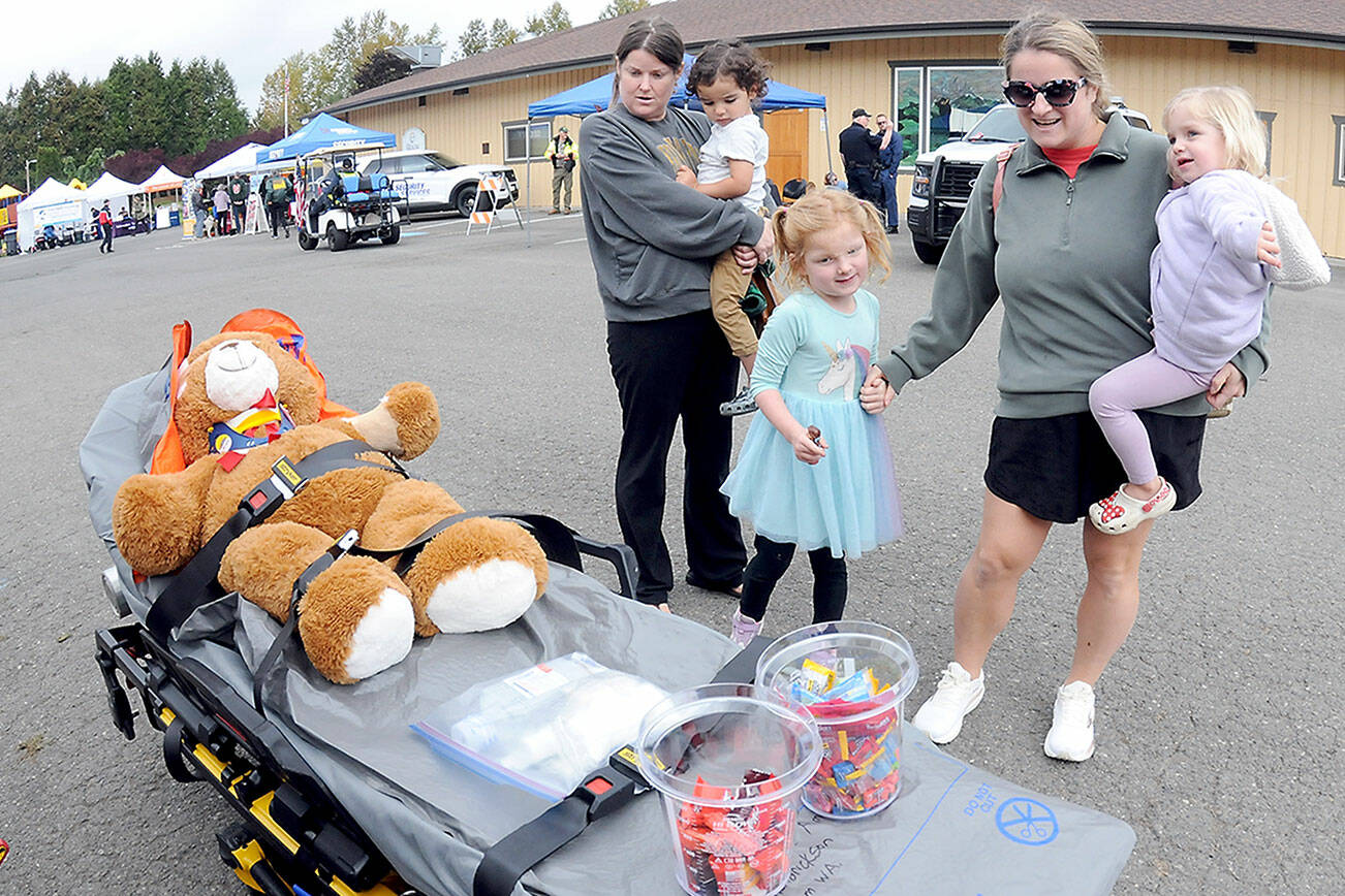 Gabriella Wolman, holding her son, Andy Wolman, 2, left, and Francesca Wolman, with daughters Lily Parker, 5, and Lucy Parker, 2, all of Sequim, examine a gurney with a stuffed bear placed on display by Olympic Ambulance during Saturday’s Safety Fair at Carrie Blake Park in Sequim. The fair, hosted by the city of Sequim, Clallam County Fire District 3 and members of the Community Emergency Response Team, featured a variety of public safety displays and demonstrations as well as workshops and lectures themed around surviving an emergency. (Keith Thorpe/Peninsula Daily News)