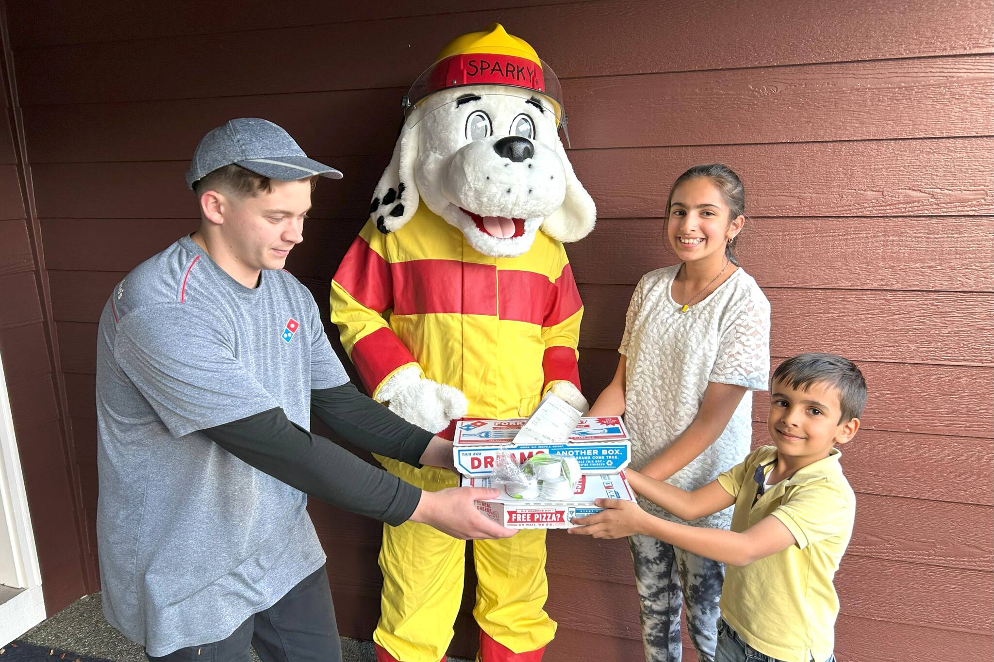 Matthew Nash/Olympic Peninsula News Group
Pizza fans Preet Saran, 10, and Jess Saran, 6, on right, receive free pizza from Domino’s delivery driver Ryan Lang and Sparky the Fire Dog on Oct. 8 as part of Fire Prevention Week efforts by Clallam County Fire District 3. Staff and volunteers, in partnership with Sequim Domino’s, checked homeowners’ smoke alarms, and if they worked, they received their orders for free.