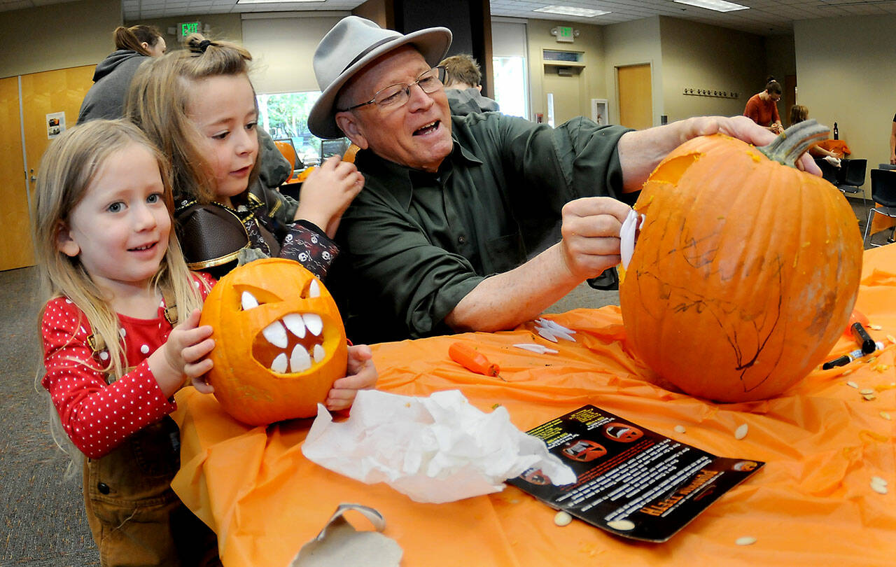 Port Angeles siblings Gwendolyn McCord, 4, left, and Brân McCord, 6, assist their grandfather, Glenn Jones, with creating a jack-o-lantern during a pumpkin-carving session on Saturday at the Port Angeles Public Library. About 40 children and their parents took part in the spooky Halloween activity. (Keith Thorpe/Peninsula Daily News)
