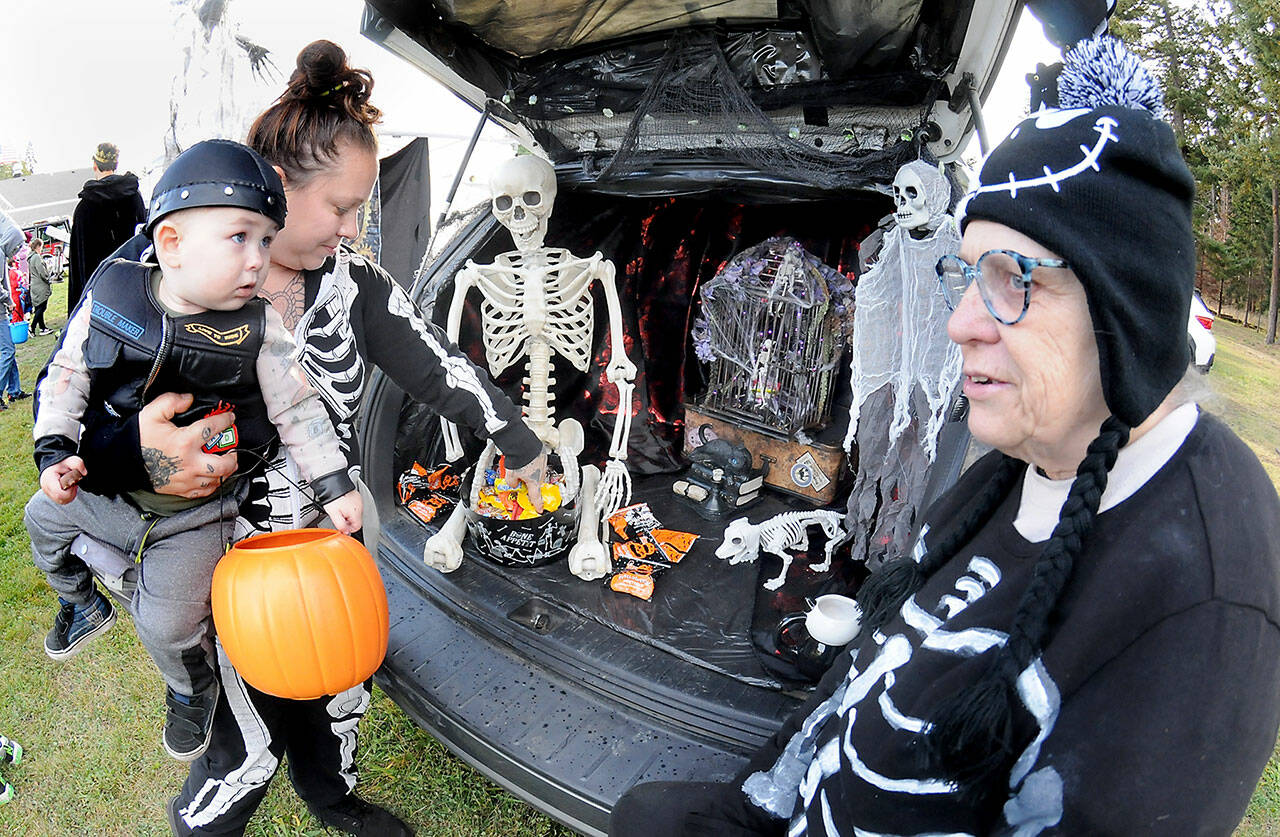 Jessica Topham of Sequim collects sweet treats for her son, Ivar Baker, 19 months, as Becky Rice looks on from her spookily decorated vehicle during Saturday’s Country Fair and Trunk or Treat at the Sequim Prairie Grange north of Carlsborg. The Halloween-themed event featured food, games, pumpkin carving and scary treats, hosted by members of the grange. (Keith Thorpe/Peninsula Daily News)