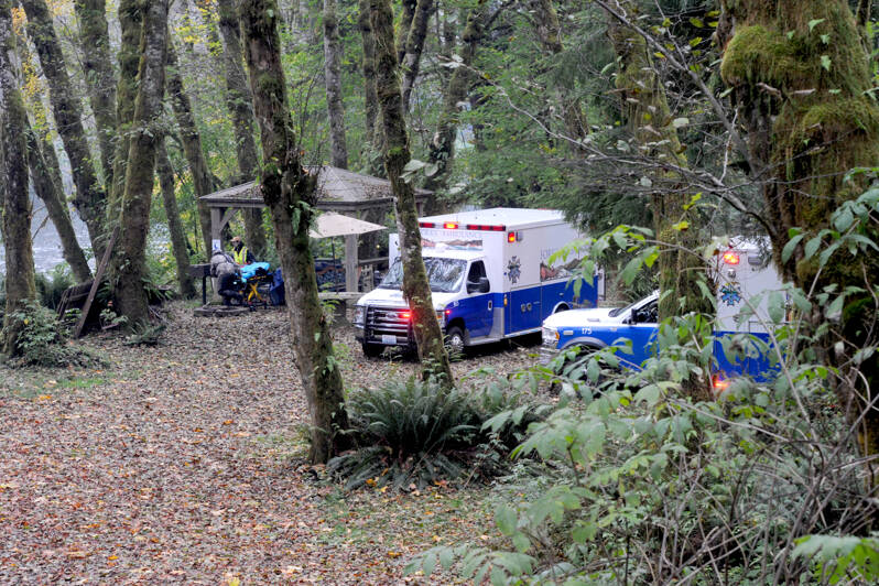 Forks medics await at the scene on the Bogachiel River near the Goodman Mainline west of Forks on Thursday afternoon after a boat overturned. Forks medics, law enforcement, Clallam County Fire District 1 and airlift all responded. Two people died and a third person is still missing, the Clallam County Sheriff’s Office said. (Lonnie Archibald/for Peninsula Daily News)