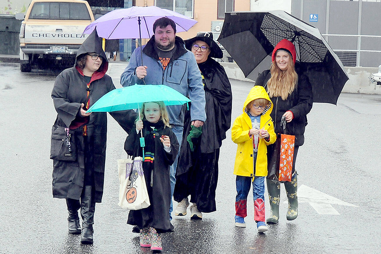 Trick or treaters and parents, from left, Angelina Simpson, Charlie Simpson, 6, Matt Simpson, Carmen Moody, Maximillion Dempsey, 7, and Holly Dempsey, all of Port Angeles, make their way through downtown Port Angeles under a moderate rain shower on Halloween Day. Many downtown merchants opened their doors with candy and treats to welcome soggy spooks, wet witches and other assorted cartoon characters in search of sweet snacks. (Keith Thorpe/Peninsula Daily News)