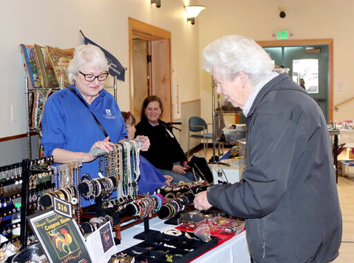 Gwyn Gallis, left, helps Pauline Olsen at the Soroptimist booth at the Port Angeles Senior and Community Center during a holiday craft fair on Saturday. Soroptimists were even selling their annual Elegant Gourmet Coupon Book for $10. They can also be purchased at Blackbird Coffee House, Fogtown Coffee Bar, Jim’s Pharmacy, Odyssey Book Store, Sweet Spot Sequim and Sequim Shoe Repair. More than a dozen vendors filled the building for holiday shoppers. (Dave Logan/for Peninsula Daily News)
