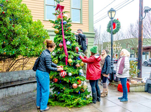 Port Townsend Main Street Program volunteers, from left, Amy Jordan, Gillian Amas and Sue Authur, and Main Street employees, Sasha Landes, on the ladder, and marketing director Eryn Smith, spend a rainy morning decorating the community Christmas tree at the Haller Fountain on Wednesday. The tree will be lit at 4 p.m. Saturday following Santa’s arrival by the Kiwanis choo choo train. (Steve Mullensky/for Peninsula Daily News)