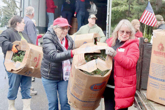 Donna Bower, left, and Kristine Konapaski, volunteers from the Michael Trebert Chapter of the Daughters of the American Revolution, unload one of the 115 boxes of Christmas wreaths and carry it to a waiting truck. (Dave Logan/For Peninsula Daily News)