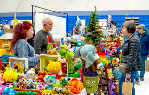Pamela and Ernie Burnett, left, talk about their craft items, Amijurmi — Japanese small crocheted stuffed yarn creatures — to Tracey Harris of Marrowstone Island on Saturday during the first of two days at the 38th annual Chimacum Arts and Crafts Show at Chimacum High School. (Steve Mullensky/for Peninsula Daily News)