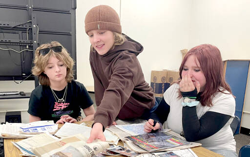 Stevens Middle School eighth-grader Linda Venuti, left, and seventh-graders Noah Larsen and Airabella Rogers pour through the contents of a time capsule found in August by electrical contractors working on the new school scheduled to open in 2028. The time capsule was buried by sixth graders in 1989. (Paula Hunt/Peninsula Daily News)