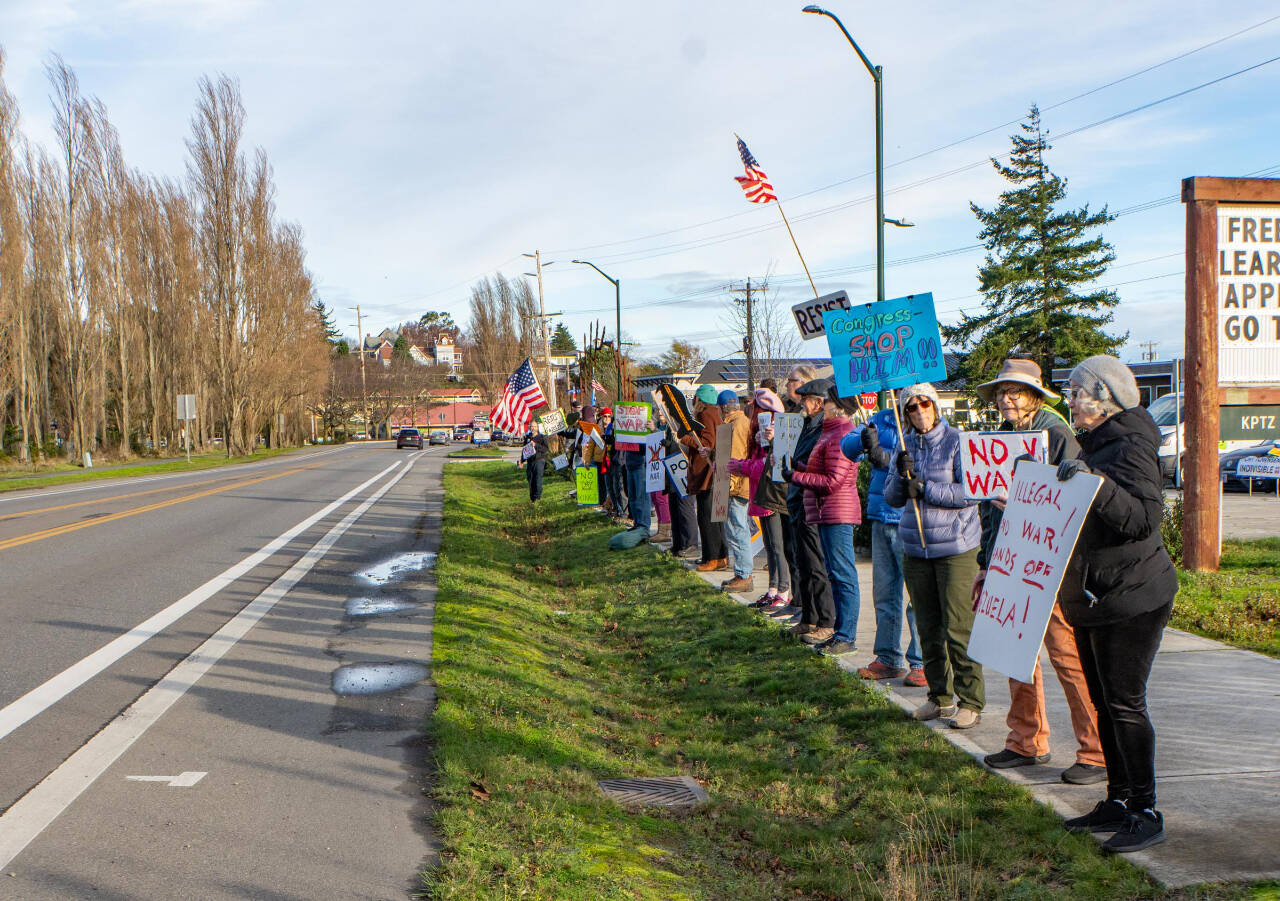 Members of Port Townsend Indivisible, a political protest group, begin to amass along Sims Way on Saturday in the first rally of 2026. The group was called to action in protest of the U.S. government and Donald Trump ousting the president of Venezuela overnight. Gina McMather, second from the right, a member of the Indivisible leadership team, led the pop-up rally. (Steve Mullensky/for Peninsula Daily News)