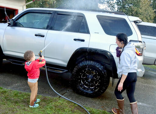 Logan Gear, 3 1/2, uses a garden hose to wash the family car in Port Angeles. His mother Rachel Gear said it was sunny and it was a chance “to get out of the house and do something constructive.” (Dave Logan/for Peninsula Daily News)