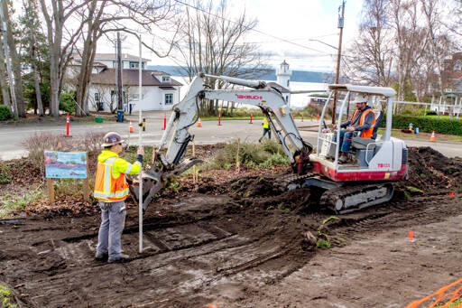Workers from Van Ness Construction in Port Hadlock, one holding a grade rod with a laser pointer, left, and another driving the backhoe, scrape dirt for a new sidewalk of civic improvements at Walker and Washington streets in Port Townsend on Thursday. The sidewalks will be poured in early February and extend down the hill on Washington Street and along Walker Street next to the pickle ball courts. (Steve Mullensky/for Peninsula Daily News)