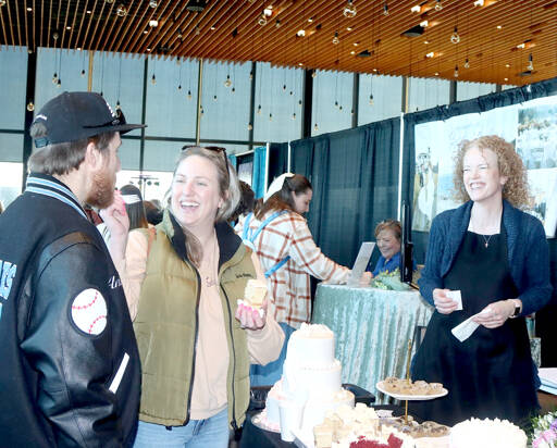 Anthony DeLeon, left, and McKenzie Koljonen, who are planning a wedding in October, practice feeding each other a piece of wedding cake during the Olympic Peninsula Wedding Expo at Field Arts & Events Hall while Selena Veach of Aunt Selena’s Bakery of Port Angeles watches with glee. More than 35 vendors presented all aspects of the wedding experience last weekend. (Dave Logan/for Peninsula Daily News)